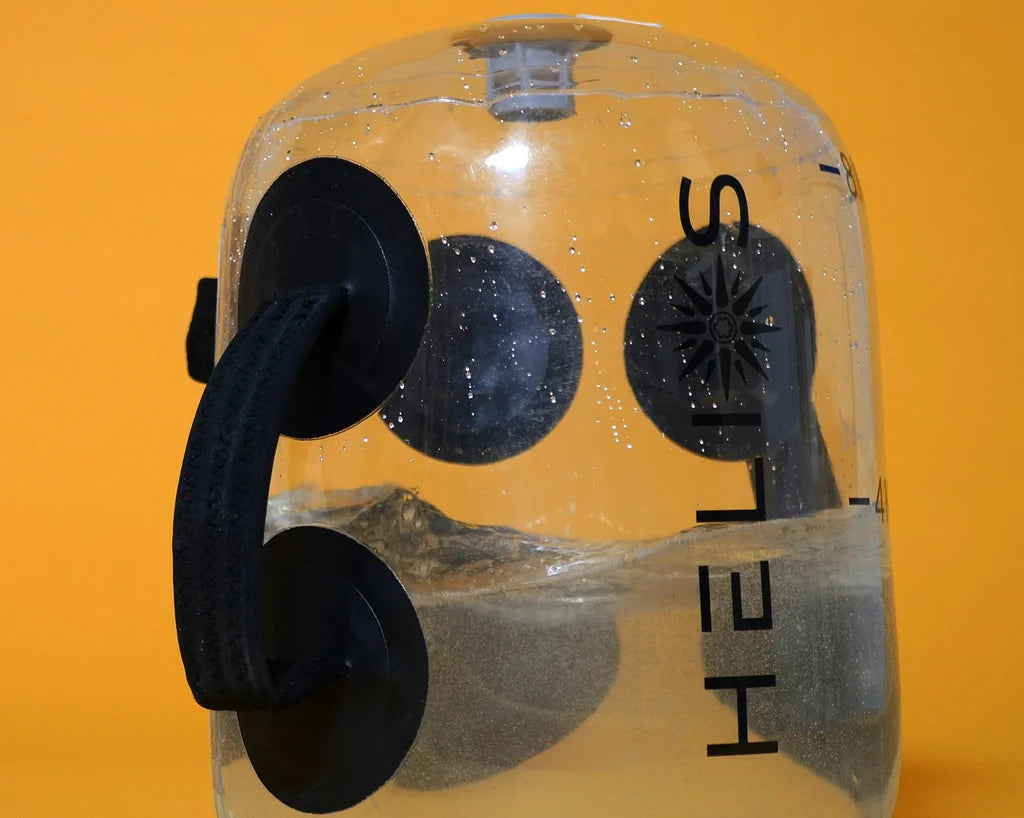 Close-up of the clear HELIOS bag part-filled with water, showing the moulded grab handles and logo